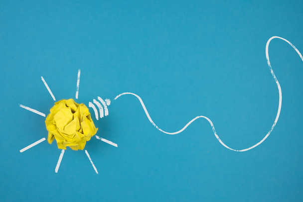 light bulb made of crumpled-up yellow paper on blue background - Fotoğraf, Görsel