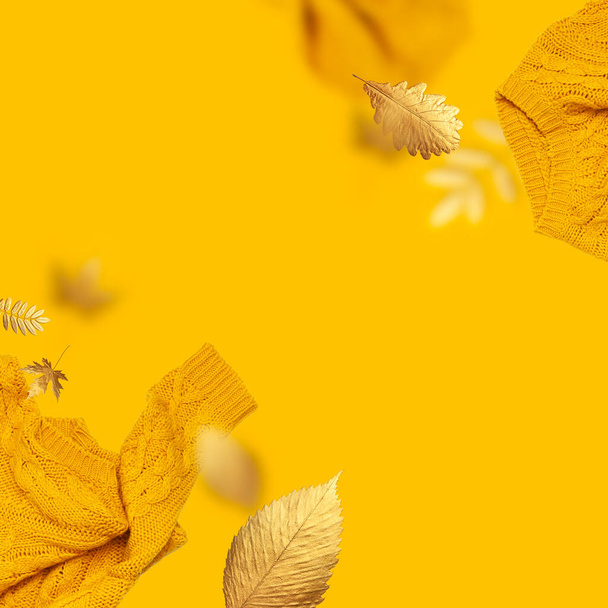 黄色の背景にオレンジ色の空飛ぶ女性のニットセーターと黄金の秋の葉で作られたフレーム。創造的な服のコンセプトは、流行の秋の冬の居心地の良いセータープルオーバージャージ。女性フラットレイファッション. - 写真・画像