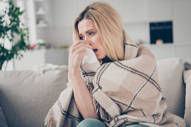 Photo of pretty suffering lady stay home quarantine covered checkered blanket hold paper napkin coronavirus infection running nose cant breathe fluently sitting sofa living room indoors - Foto, imagen