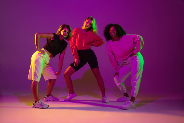 Sportive girls dancing hip-hop in stylish clothes on gradient background at dance hall in neon light - Fotoğraf, Görsel