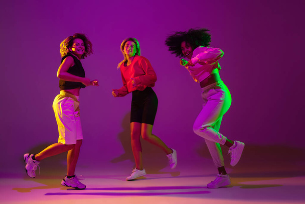 Sportive girls dancing hip-hop in stylish clothes on gradient background at dance hall in neon light - 写真・画像