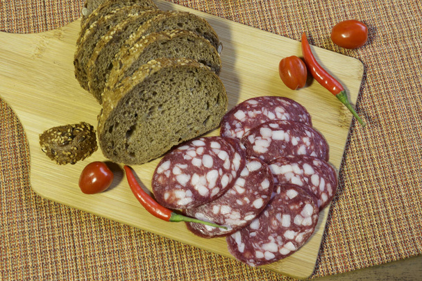 Σαλάμι λουκάνικο και ψωμί για σάντουιτς, φέτες σε ξύλο κοπής. - Φωτογραφία, εικόνα