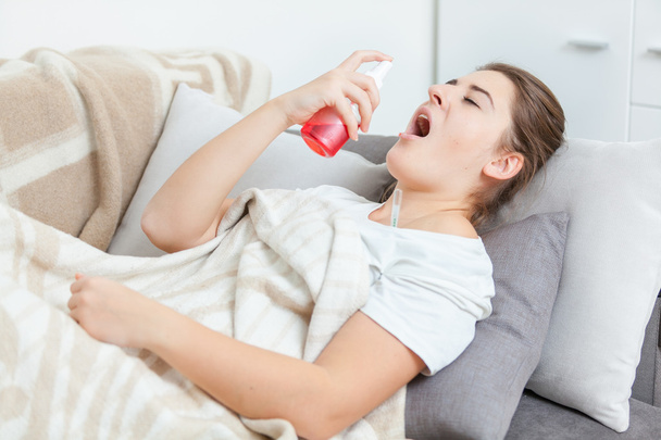 Mulher doente deitada na sala de estar e usando spray de garganta
 - Foto, Imagem