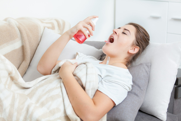 Woman using throat spray while lying on couch - Zdjęcie, obraz