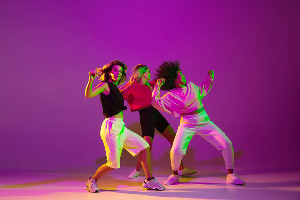 Sportive girls dancing hip-hop in stylish clothes on gradient background at dance hall in neon light - Foto, imagen