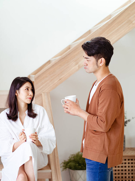 Young asian woman and man are enjoying spending time together at home with cup of coffee in hands. - Fotó, kép