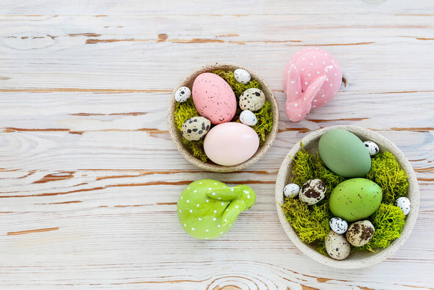 Easter decorations with eggs, moss and ceramic figurines on white wooden table. Festive time - Fotoğraf, Görsel