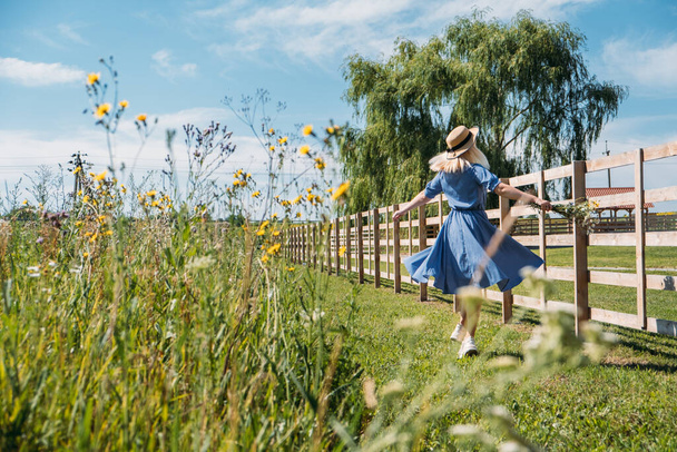Cottagecore Farmcore Countrycore αισθητική, φρέσκο αέρα, ύπαιθρο, αργή ζωή, ποιμαντική ζωή, υπαίθρια πικνίκ, φορώντας ρούχα γιαγιά. Νεαρή κοπέλα με ψάθινο καπέλο με λουλούδια περπατάει στη φάρμα.. - Φωτογραφία, εικόνα