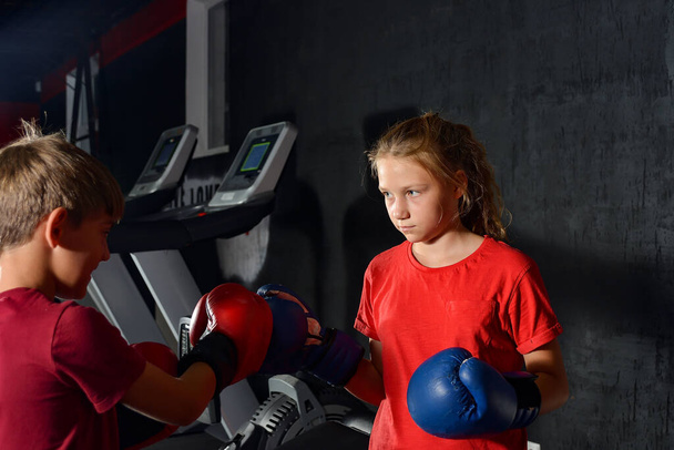 Junge und Mädchen in Boxhandschuhen boxen in der Sporthalle miteinander. Kinder boxen. - Foto, Bild