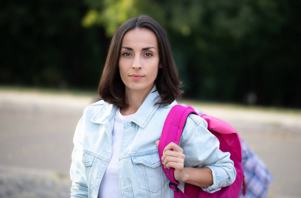 Beautiful young modern student girl with a backpack is looking on camera outdoors - Photo, image