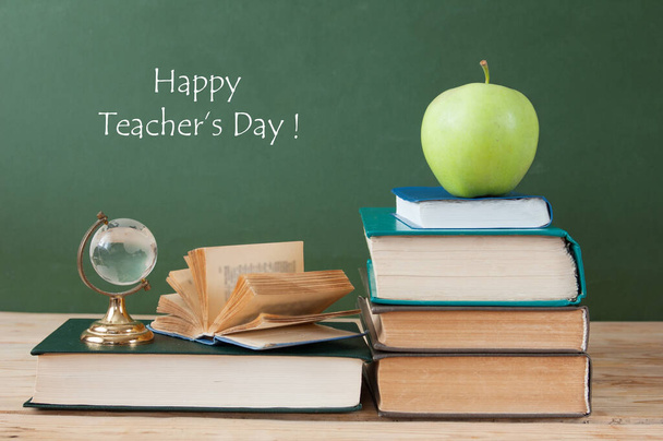 Book pile with apple, globe, pencils and sharpener on the school blackboard. Teacher's day concept - Photo, image