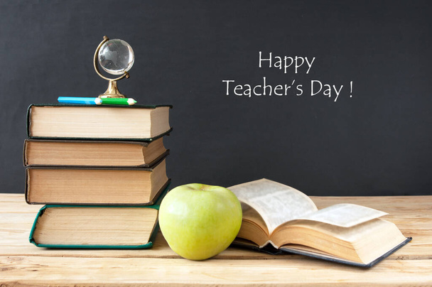 Boek stapel met appel, bol, potloden en slijper op het schoolbord. Lerarendagconcept - Foto, afbeelding
