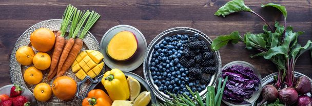 Narrow view of fresh fruits and vegetables in rainbow colours against a dark wooden background. - Photo, Image