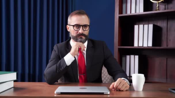 De baas, wiens gezicht vol baard zat, nam een bril af met een serieuze uitdrukking.. - Video