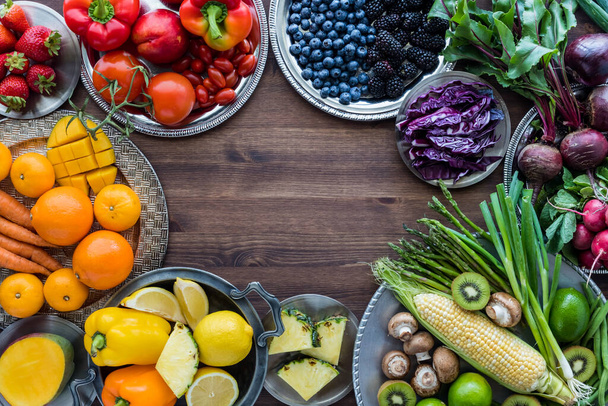 Varias frutas y verduras en platos de metal en colores arcoíris y dispuestos en un borde con espacio de copia en el centro. - Foto, imagen