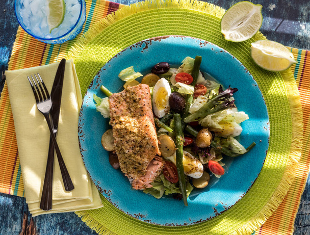Nicoise-Salat mit Lachsfilet mit grellem Sonnenlicht, das durch Jalousien strömt. - Foto, Bild