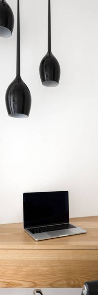 Vertical panorama of study area with computer on stylish wooden desk in white room with black pendant lamps - Fotó, kép