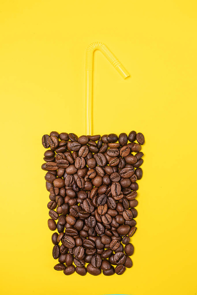 Magas üveg, sárga hátterű kávébabbal bélelt. Fent - egy sárga tubulus. A kávéalapú italok kreatív koncepciója. Felülnézet, lapos fekvés, másolás. - Fotó, kép