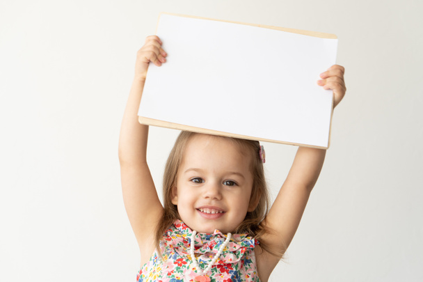 Boldog mosolygós lány kezében fehér papírlap hely szöveges, másolja helyet a szobában. Anyák napja, rajz, home art concept. - Fotó, kép