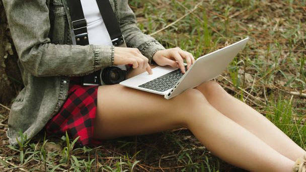 Mujer joven, escribiendo en el teclado del ordenador portátil mientras se encuentra en la hierba en el parque - Foto, imagen