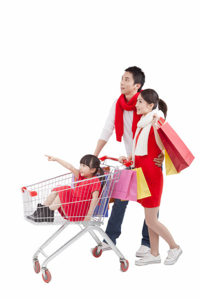 	Portrait of daughter sitting in shopping cart,father pushing shopping cart,mother holding shopping bags 	 - Foto, imagen