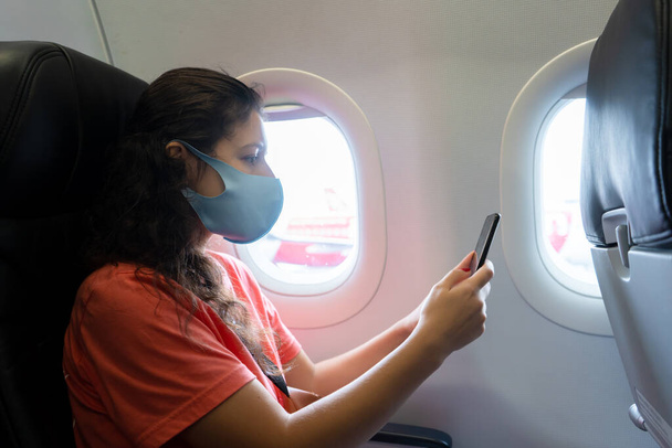 A girl in a medical mask on her face during a flight in the cabin. Air travel during a pandemic. - Fotó, kép