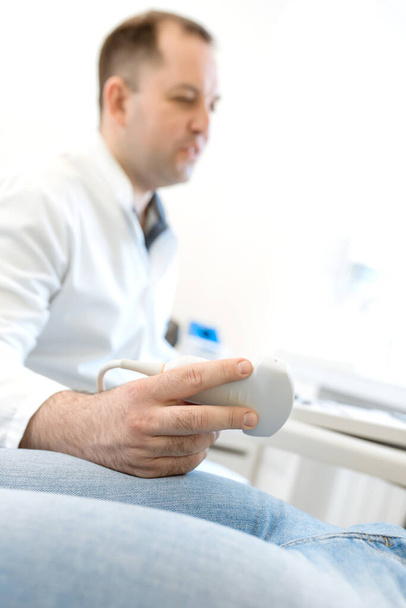 Male doctor holding an ultrasound diagnostic probe. Focus on the hand, the doctor is blurred - Foto, Bild