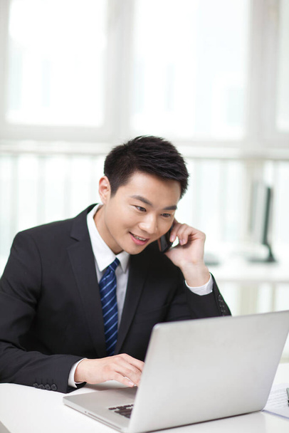 	Portrait of businessman sitting at desk and using cell phone	 - Photo, image