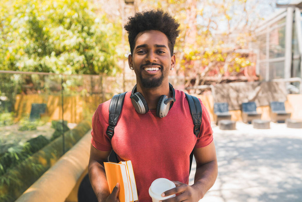 Portrait of young afro university student holding his books and looking at camera, outdoors in the campus. Education and lifestyle concept. - Photo, image