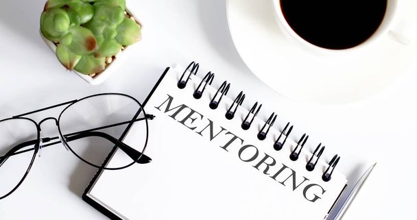 Business concept - Top view notebook di scrittura MENTORING con bicchieri e tazza di caffè su sfondo bianco - Foto, immagini