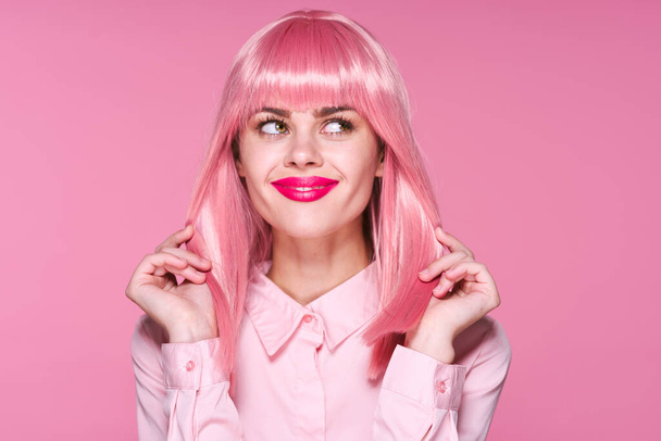 Студийный снимок Молодая девушка в розовом парике смотрит в сторону на розовом фоне - Фото, изображение