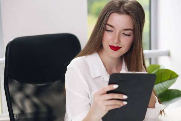 Portrait of young businesswoman wearing white shirt sitting in modern office with laptop - Fotografie, Obrázek