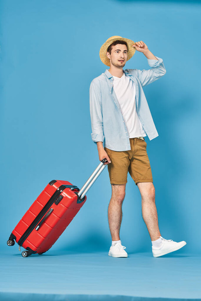 Studio shot of young man tourist pulling  red suitcase - Fotó, kép