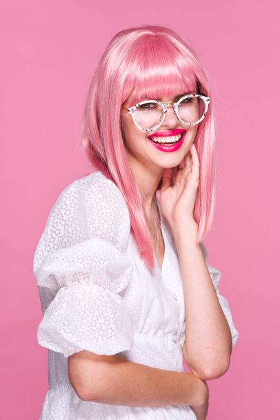 Grabado en estudio. Joven chica sonriente en peluca rosa y gafas sobre fondo rosa - Foto, imagen