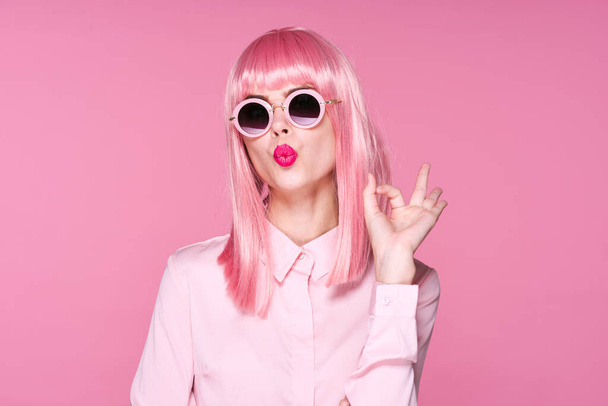 Stúdió felvétel. fiatal lány rózsaszín paróka és napszemüveg fúj csók rózsaszín háttér - Fotó, kép