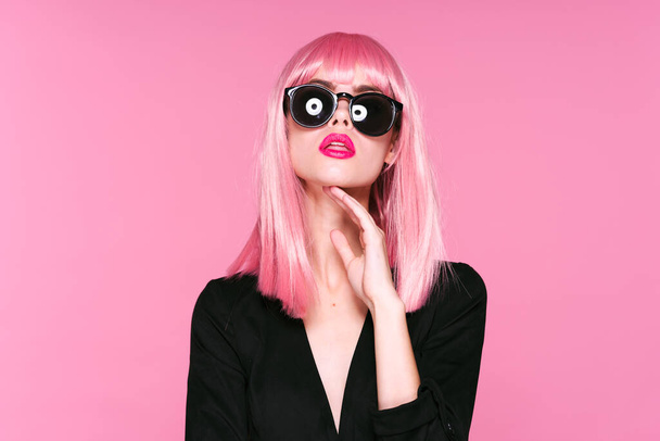 Grabado en estudio. Chica joven con peluca rosa y gafas de sol sobre fondo rosa - Foto, Imagen