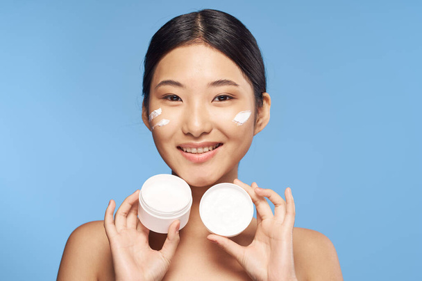 Giovane bella sorridente asiatico donna holding crema isolato  - Foto, immagini