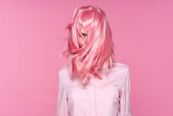 Studio shot. Young girl in pink wig with blowing hair on pink background - Photo, Image