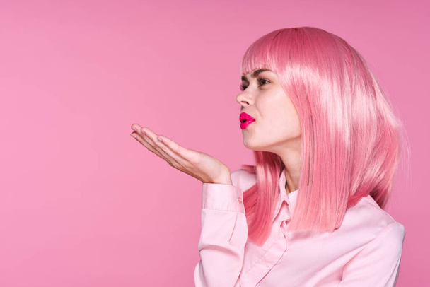 Colpo in studio. Giovane ragazza in rosa parrucca soffiaggio bacio su sfondo rosa - Foto, immagini