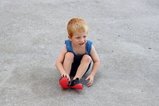 Surullinen poika, jolla on hiertymiä jalassaan. Lapsi loukkasi polvensa asfaltilla. Kömpelö lapsi. hiertymät - Valokuva, kuva
