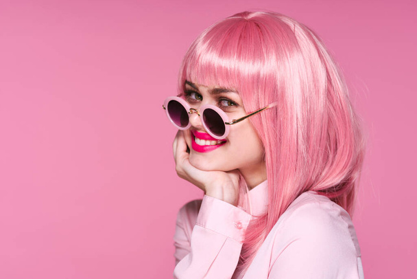 Charmante Frau mit pinkfarbener Perücke und Sonnenbrille auf rosa Hintergrund  - Foto, Bild