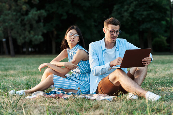 młodzi studenci z laptopem na trawniku  - Zdjęcie, obraz