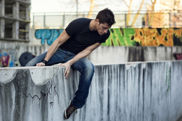 Young man sitting and balancing on wall, looking down - Valokuva, kuva