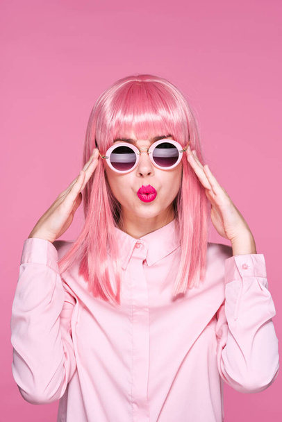 hermosa mujer en peluca rosa y gafas de sol sobre fondo rosa  - Foto, Imagen