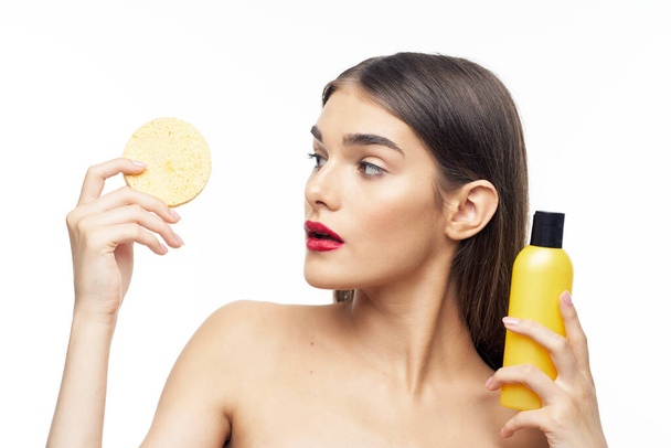 jovem mulher bonita segurando esponja e produto de beleza para limpar a pele no estúdio  - Foto, Imagem