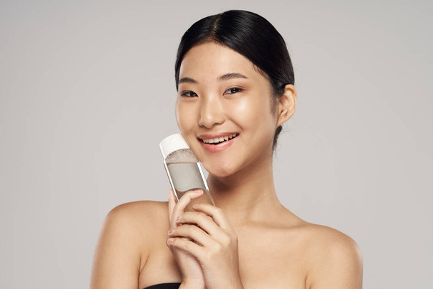 Young beautiful asian woman with skincare product   in studio on isolated background - Фото, изображение