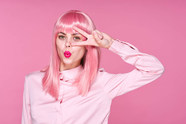 Een studio opname. jong meisje in roze pruik gebaar op roze achtergrond - Foto, afbeelding