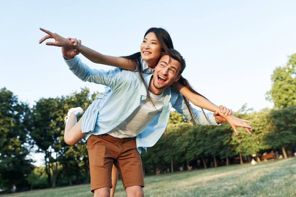 Young beautiful couple   in summer park. man giving woman piggyback ride - 写真・画像