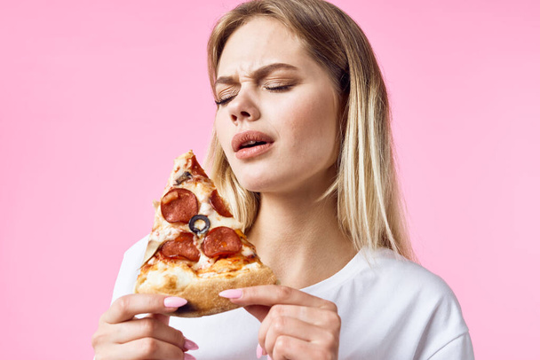 Pembe arka planda pizza yiyen genç ve güzel bir kadın.  - Fotoğraf, Görsel