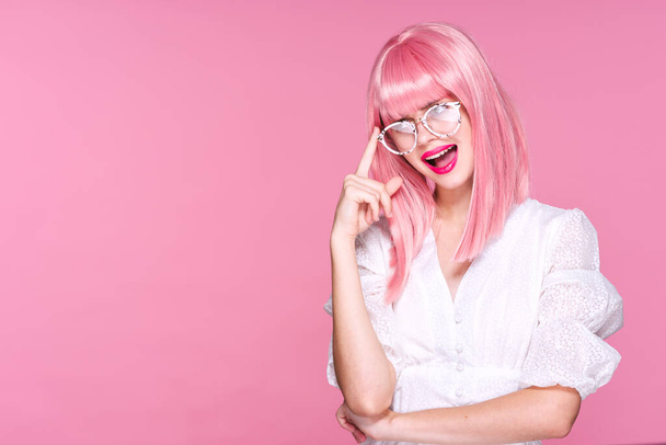 Jeune femme en perruque rose et lunettes en studio sur fond rose - Photo, image